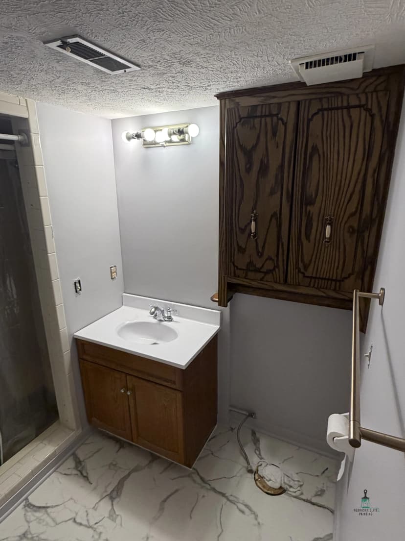 Renovated bathroom with wooden cabinet, sink, and tiled floor, featuring a shower area.