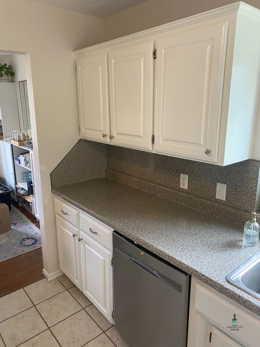 Modern kitchen with white cabinets and granite countertops, featuring a sleek dishwasher.